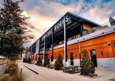 The restored Armature Works streetcar barn in Tampa at dusk, with its brick facade, steel canopy and picnic tables along the walkway.