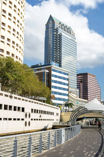 The Tampa Riverwalk curving beside the Hillsborough River, with the downtown skyline and a shaded walkway canopy behind.