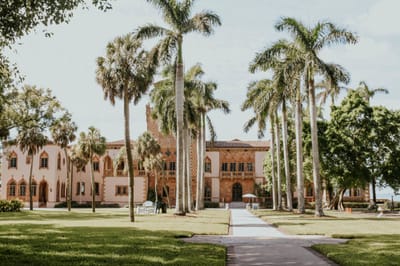Ca' d'Zan, the 1920s Ringling mansion in Sarasota, Florida, seen across a lawn from a walkway lined with royal palms.