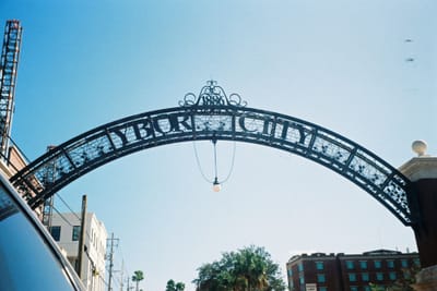 The wrought-iron Ybor City gateway arch in Tampa, lettered YBOR CITY with the date 1886 in its scrollwork crown, photographed from below against a clear sky.